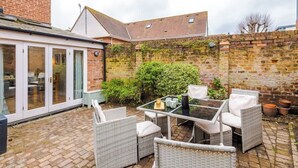 A patio area with wicker furniture, a glass table, and a brick wall. - NEW! Spacious 2-Bed Home, Amazing Location! (Chester)