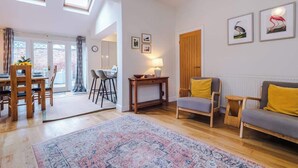 A spacious living area with a wooden dining table, a sofa, and a patterned rug. There are skylights, a door, and framed pictures on the wall. - NEW! Spacious 2-Bed Home, Amazing Location! (Chester)