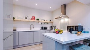 A modern kitchen with white cabinets, a central island, a stainless steel range hood, and a variety of appliances including a microwave and coffee maker. - NEW! Spacious 2-Bed Home, Amazing Location! (Chester)