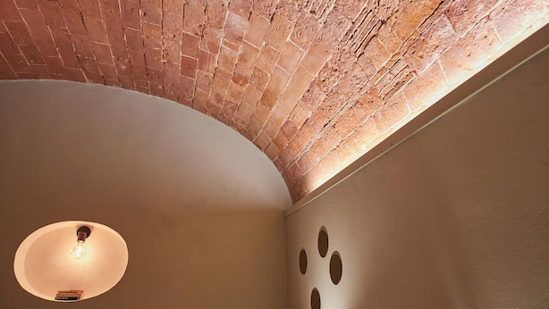 Een kamer met een bakstenen plafond, een ronde lamp en ronde uitsparingen in de muur.