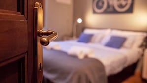 Een hotelkamer met een houten deur, een bed met een wit- en blauwe dekbedovertrek, en een fietsaffiche hangend aan de muur.