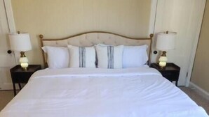A large bed with a tufted headboard, two bedside tables with lamps, and a blue patterned rug.