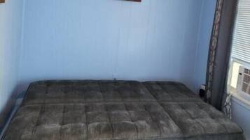 Une chambre avec un lit simple, un tableau encadré au mur et une fenêtre avec des rideaux.