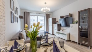 A modern living room with a dining area set for a meal, a flat-screen TV, and a bookshelf.