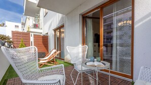 A patio with white wicker chairs and a table, a wooden deck, and a view of a building with balconies.