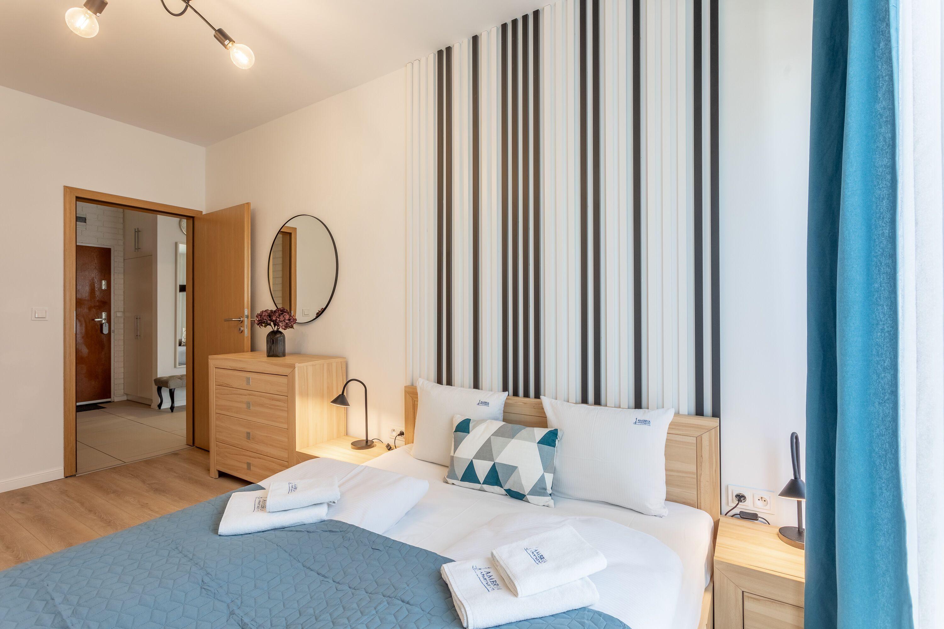Une chambre d’hôtel moderne avec un grand lit, une commode en bois, un miroir et un mur à rayures.
