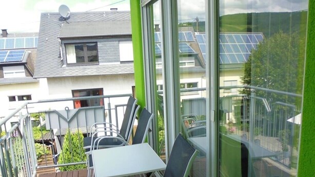 Un balcon avec une table et des chaises, de grandes fenêtres et des panneaux solaires sur le toit.