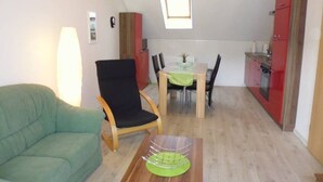 Un espace de vie compact comprenant un canapé, une table à manger, des chaises, un coin cuisine et une petite fenêtre.