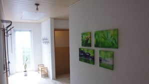 Un couloir avec un plafond blanc, une plante en pot et un banc en bois. Quatre tableaux encadrés sont accrochés au mur.