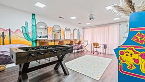 Une pièce avec une table de baby-foot, une fresque murale colorée, une boule à facettes et un grand miroir.