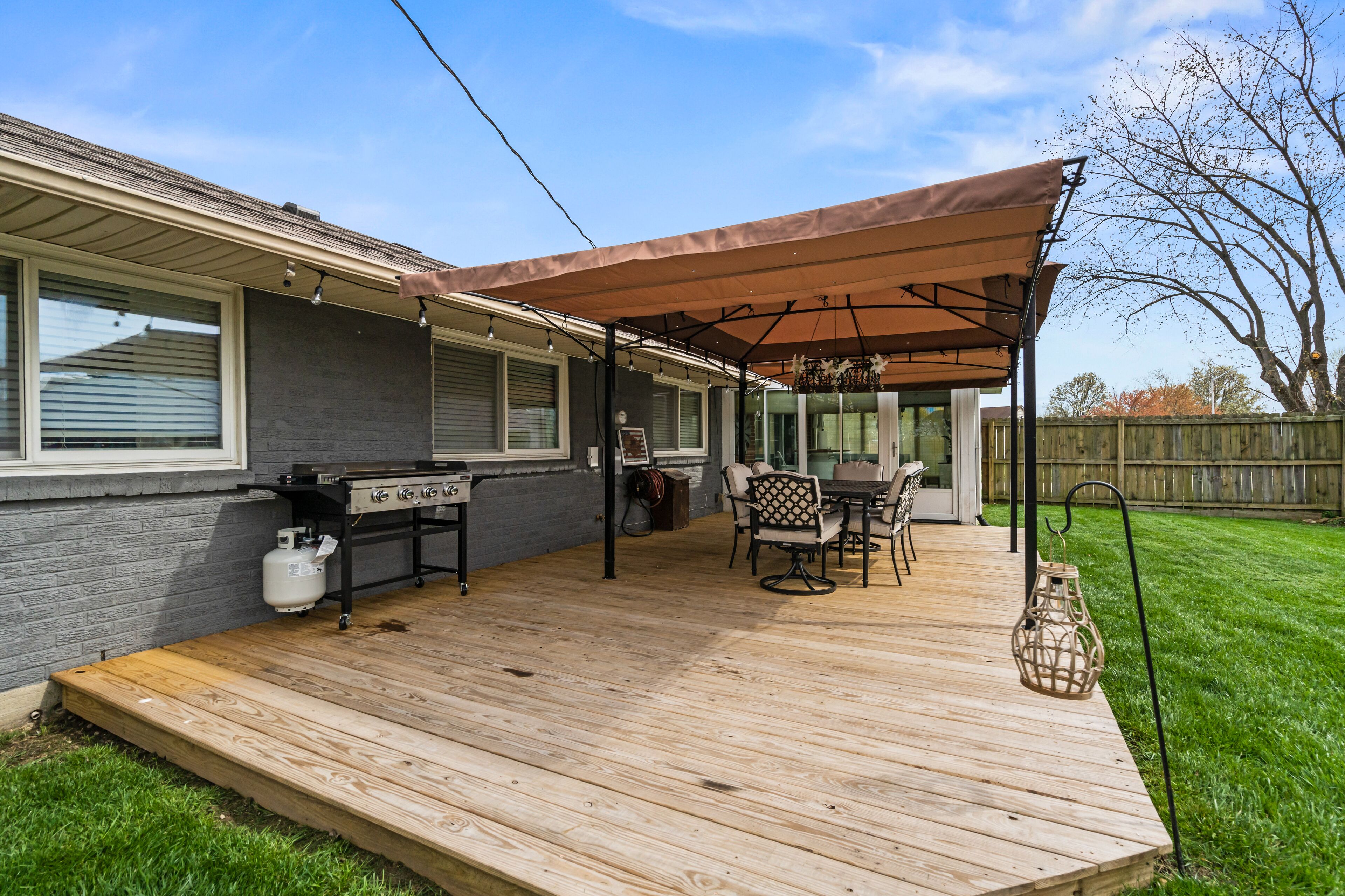 A covered patio with a grill, outdoor table and chairs, and a wooden deck.
