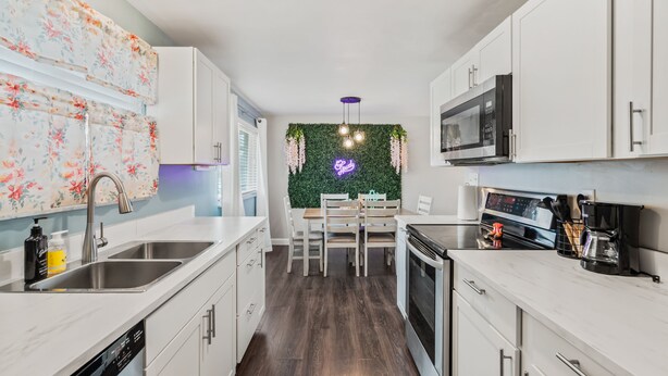 Une cuisine moderne avec des meubles blancs, des appareils en acier inoxydable et un mur vert orné de plantes suspendues.