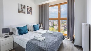 Una habitación de hotel moderna con una cama grande, una mesita de noche, una lámpara y vistas a la ciudad a través de un ventanal amplio.