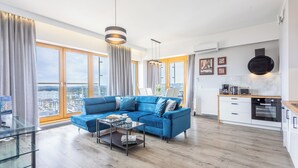 Una sala de estar moderna con un sofá seccional azul, una mesa de centro de vidrio y grandes ventanales con vistas a la ciudad.