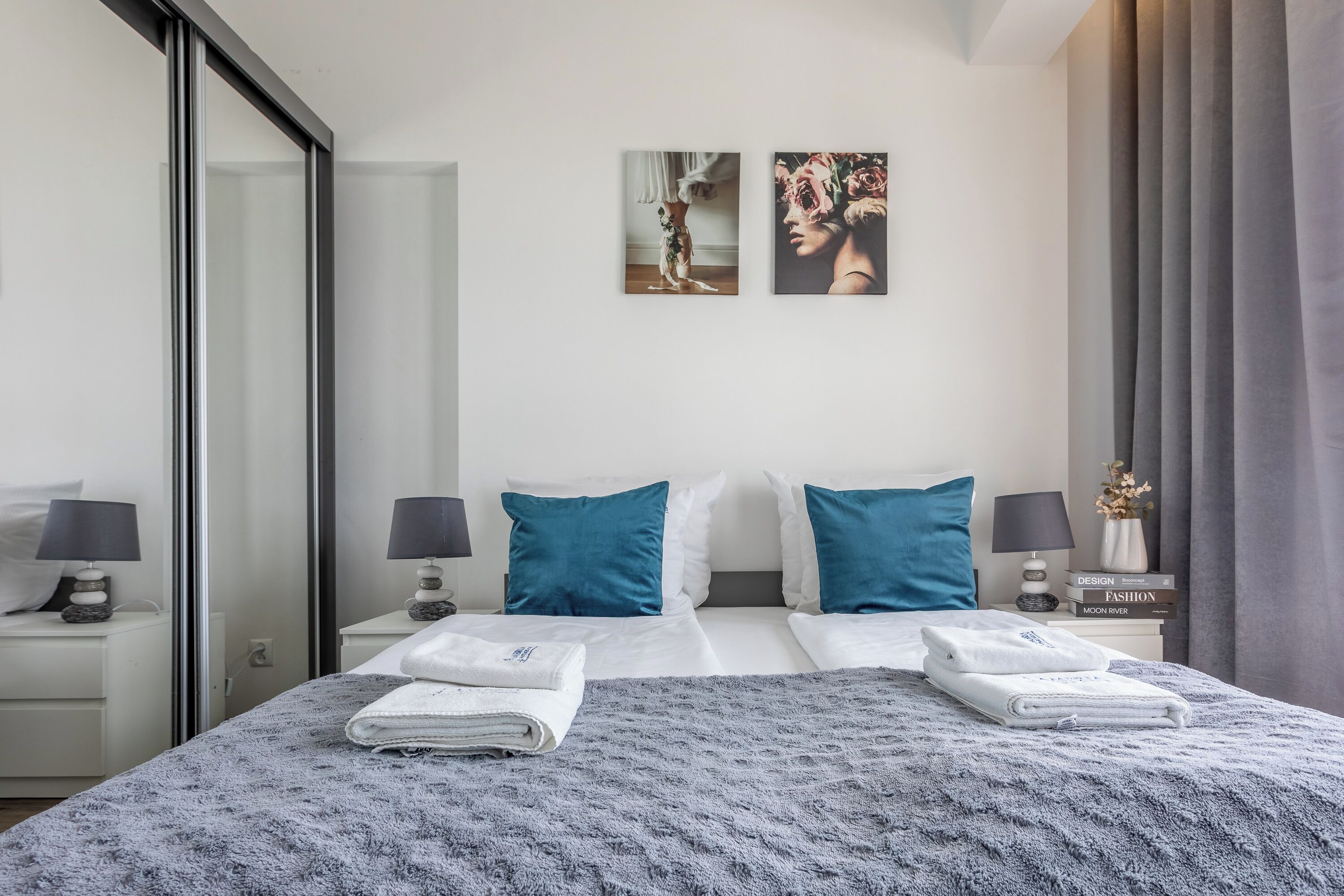 Een moderne hotelkamer met een groot bed, twee kussens, een nachtkastje met een lamp en twee kunstwerken aan de muur.