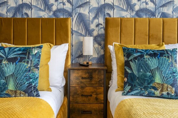 A room with two beds, each with a yellow headboard and a nightstand between them.