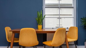 A dining area with a wooden table and four yellow chairs, a potted plant, and a window with a view of a building. - BRAND NEW The Palms: Luxury 4-6ppl Apartment (Greater London)