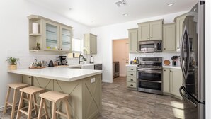 A modern kitchen with a central island, bar stools, built-in appliances, and light-colored cabinetry. - Large with King Beds, Movie & Game Room, Saloon & Close to Park (Yucca Valley)