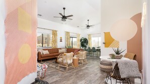 A modern living room with a sofa, chairs, a dining table, and ceiling fans. - Large with King Beds, Movie & Game Room, Saloon & Close to Park (Yucca Valley)