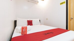 Ein ordentlich bezogenes Bett mit weißer und roter Bettwäsche, ein Handtuch mit RedDoorz-Logo und ein 'Rauchen verboten'-Schild an der Wand.