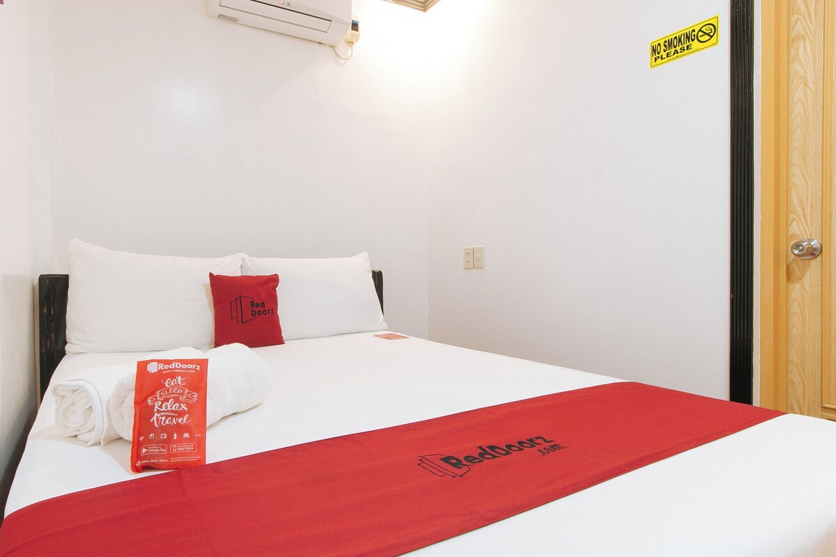Un lit bien fait, avec une literie blanche et rouge, une serviette de la marque RedDoorz et un panneau « Interdiction de fumer » accroché au mur.