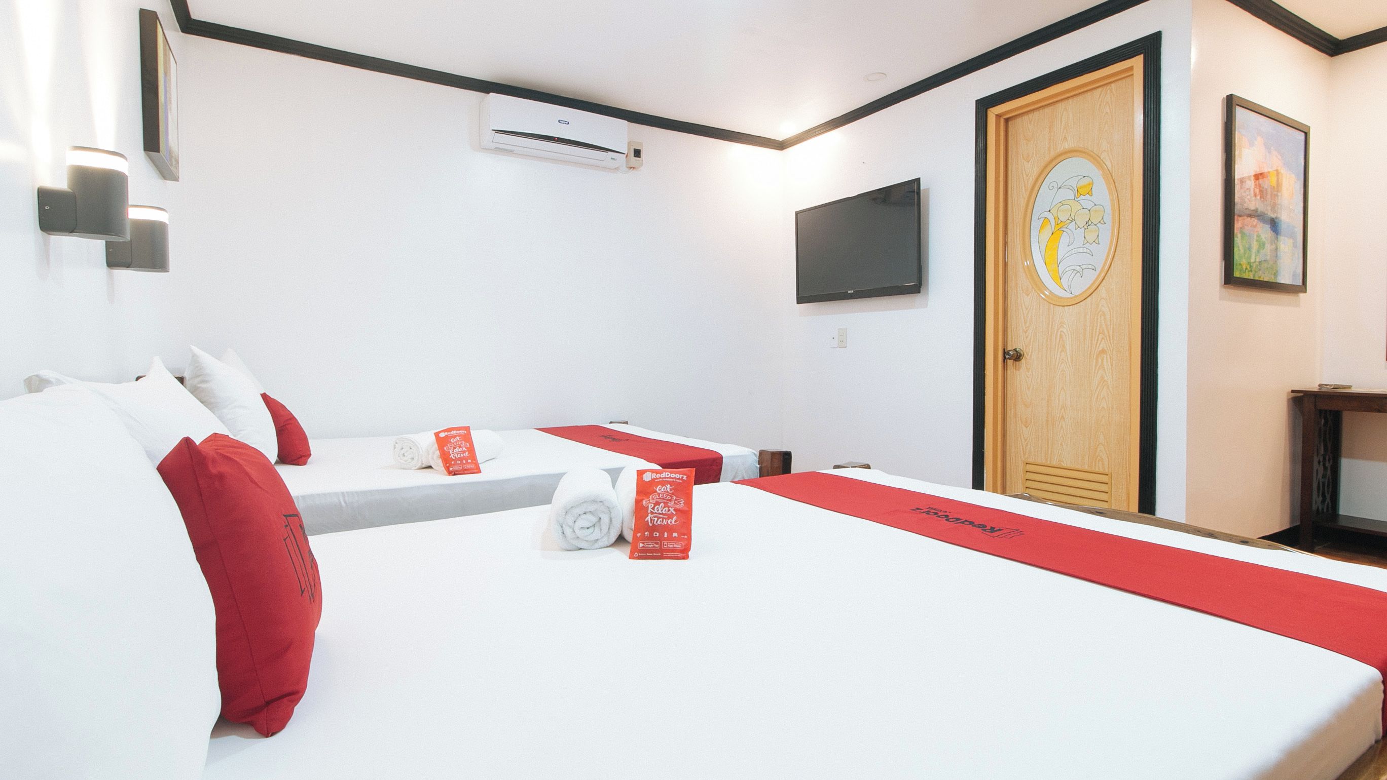 A hotel room with two beds, a TV, a door with a circular design, and a wall-mounted air conditioner.