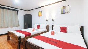 Une chambre d’hôtel avec deux lits simples, chacun recouvert d’une couverture rouge et agrémenté d’oreillers, une armoire en bois, une fenêtre avec des rideaux et un luminaire fixé au mur.