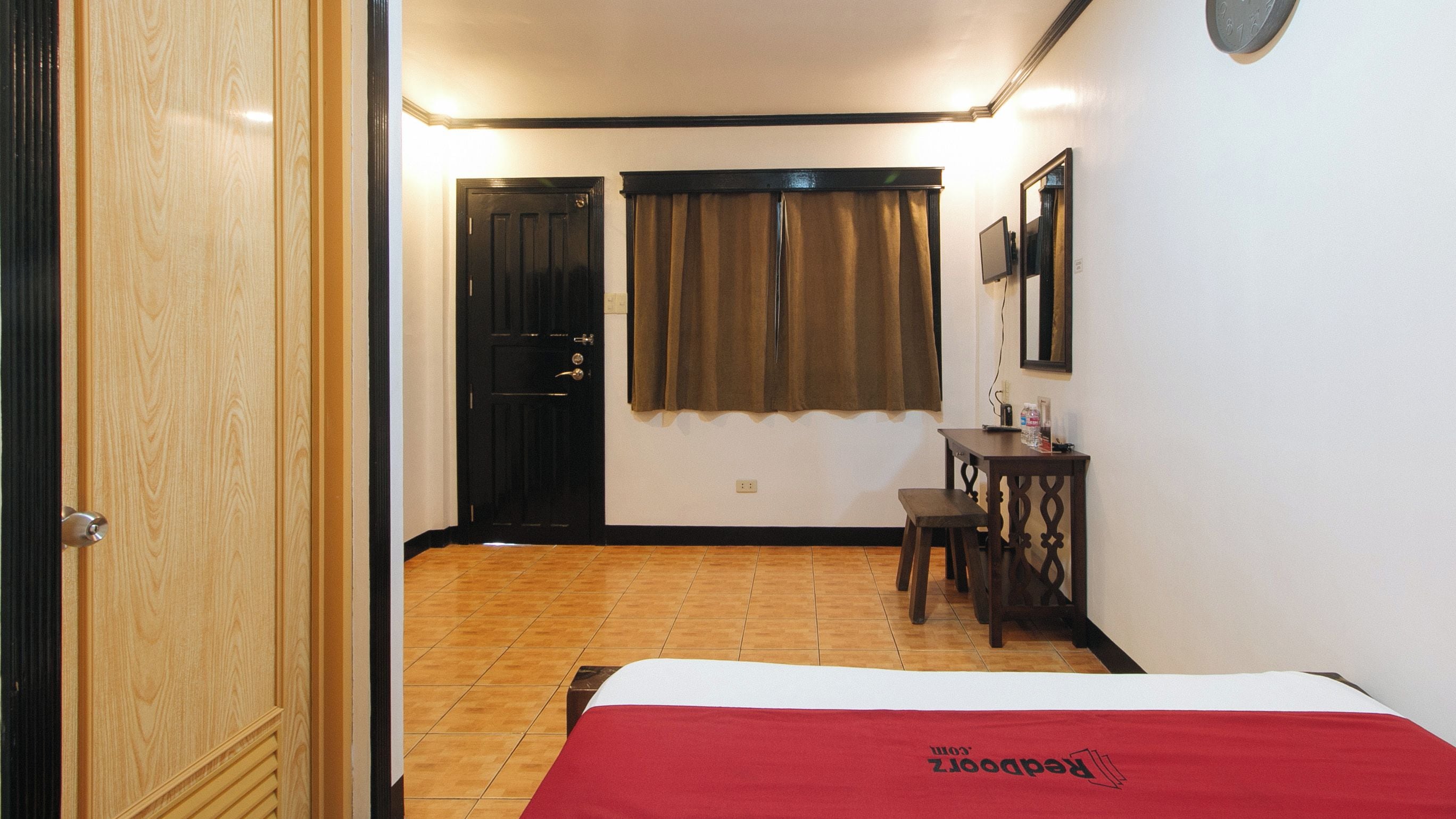 Habitación de hotel con cama, escritorio, silla, ventana con cortinas y puerta.
