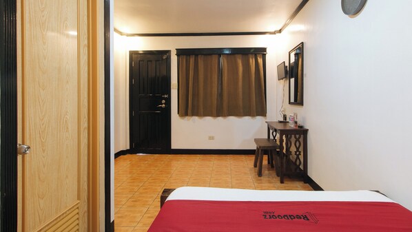 Ein Hotelzimmer mit Bett, Schreibtisch, Stuhl, einem Fenster mit Vorhängen und einer Tür.