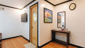 Um corredor com porta de madeira, televisão de tela plana, um quadro, um espelho e um aparador com água engarrafada.