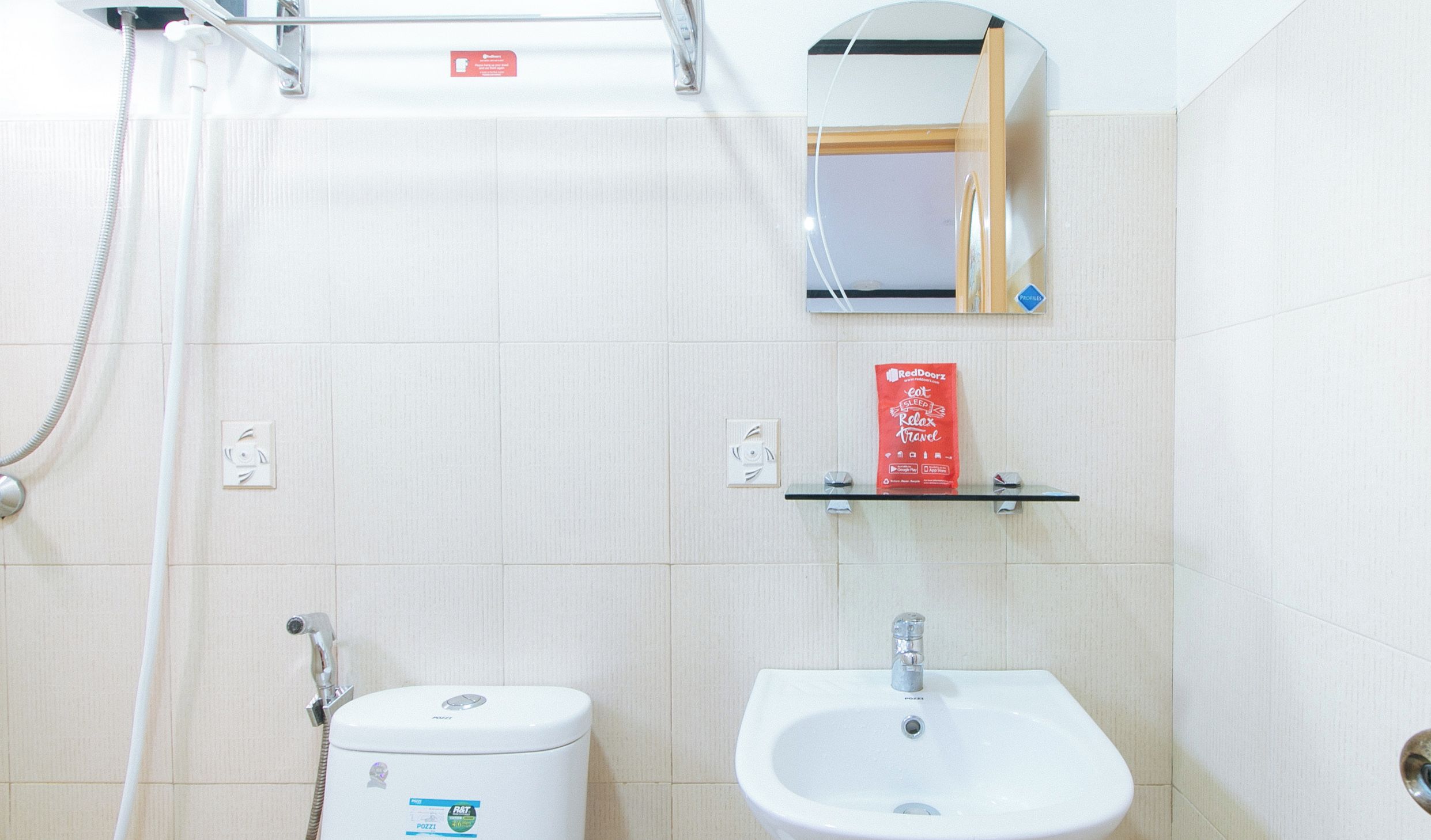 Un bagno con toilette, lavandino e doccia. C'è una borsa RedDoorz sullo scaffale.