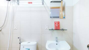 Un bagno con toilette, lavandino e doccia. C'è una borsa RedDoorz sullo scaffale.