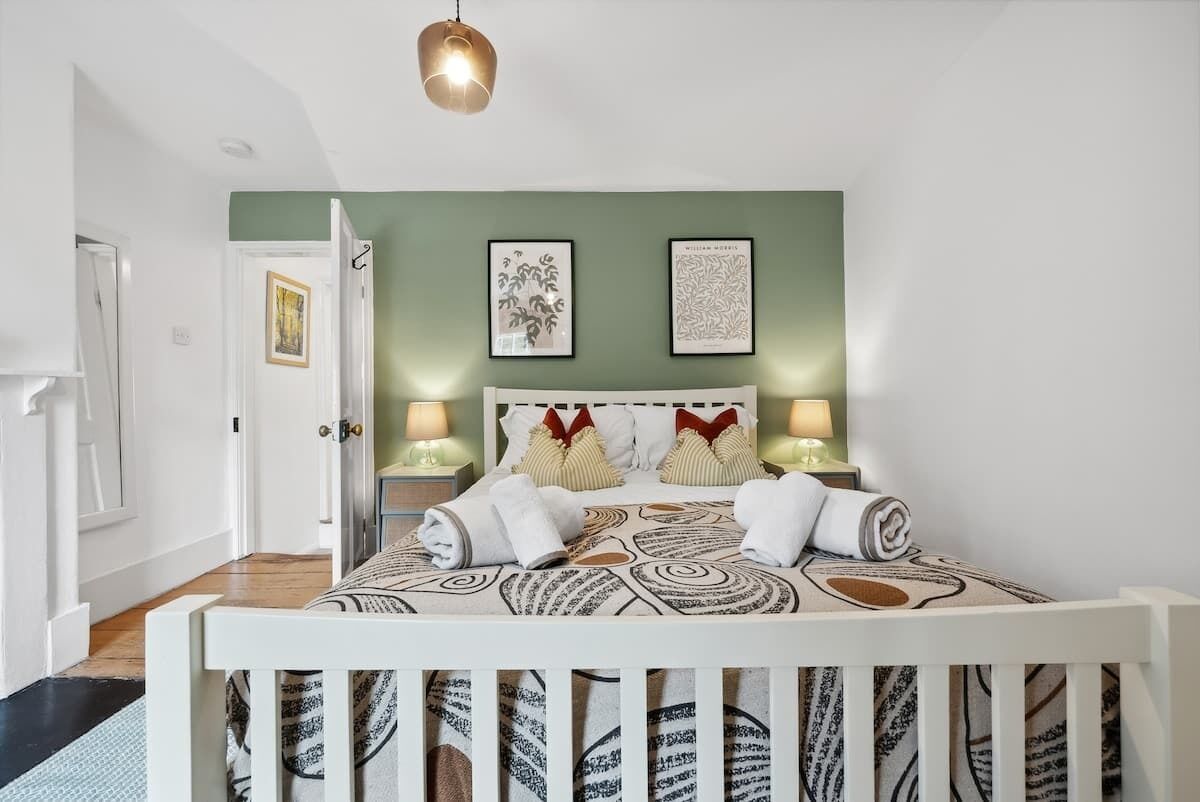 Ein ordentlich eingerichtetes Schlafzimmer mit einem Bett, zwei Nachttischen, einer Pendelleuchte und gerahmten Kunstwerken an der Wand.