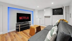 Un soggiorno moderno con televisore a schermo piatto, pavimento in legno, un divano grigio e mobili bianchi.