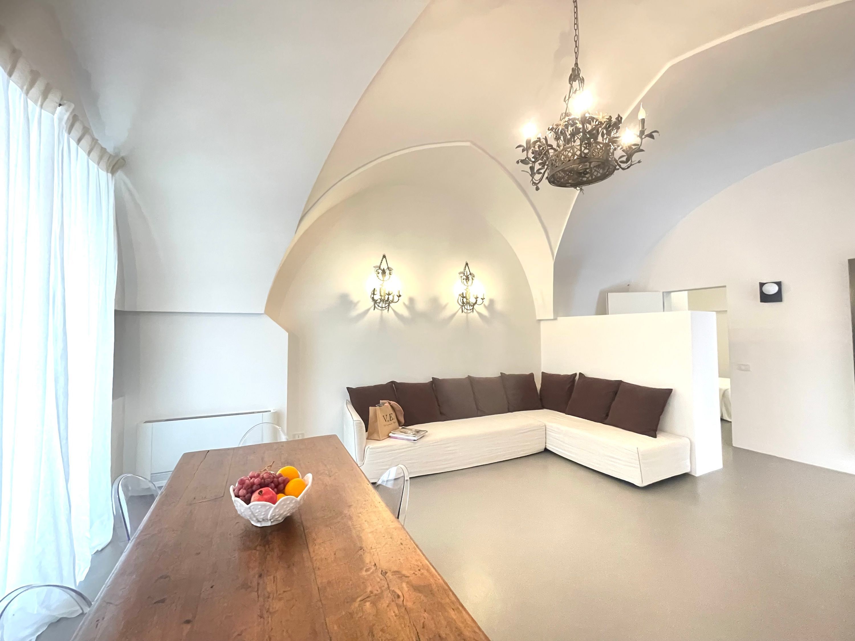 A modern interior with a wooden dining table, a white sofa, and a chandelier.