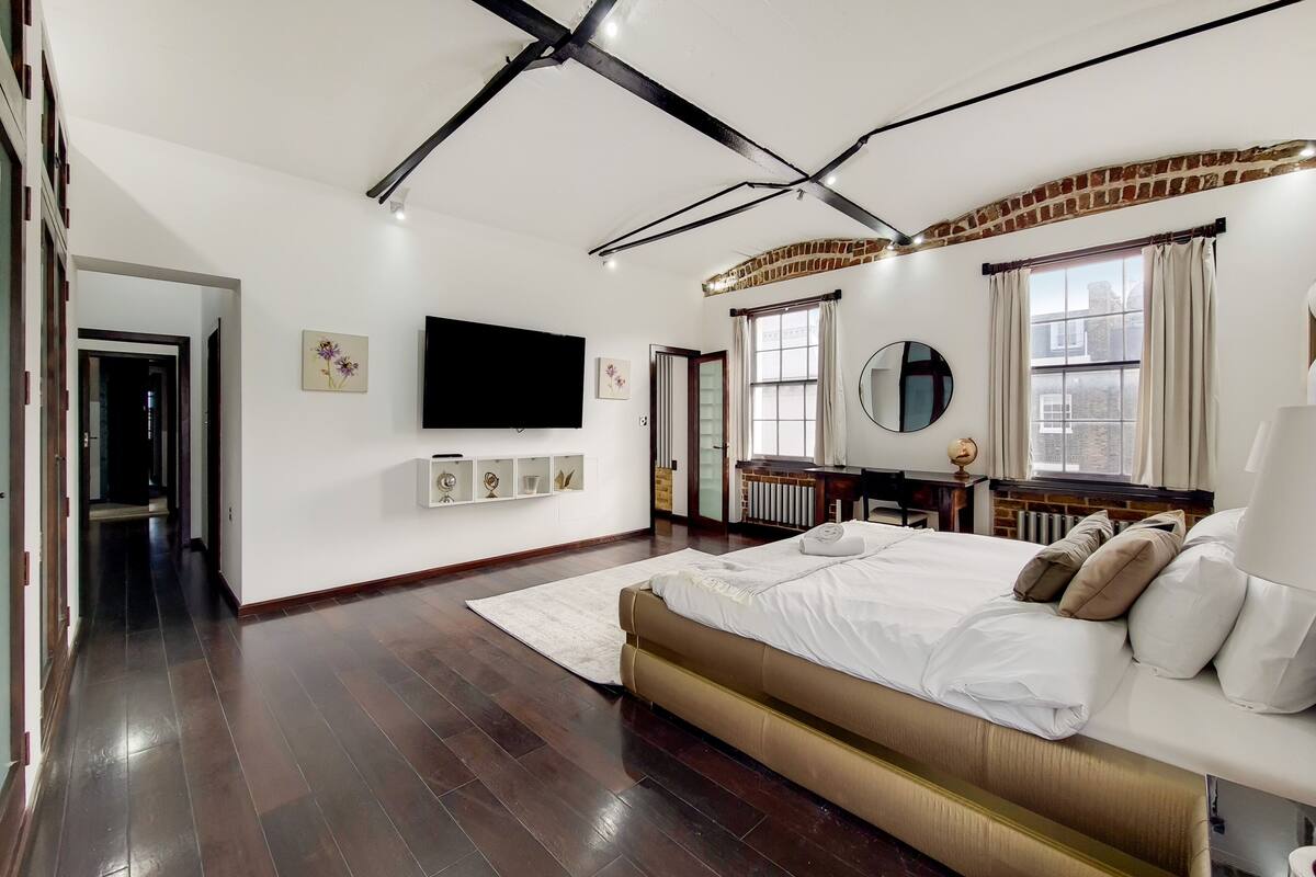 A modern bedroom with a large bed, a flat-screen TV, and a brick accent wall.