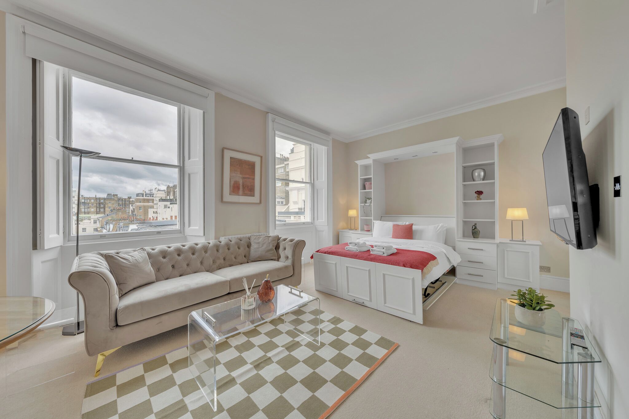 A modern bedroom with a large window, a bed with a red blanket, a white bedside table, and a TV mounted on the wall.