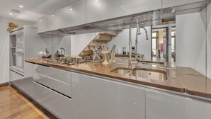 A modern kitchen with a stainless steel sink, a built-in oven, and a wooden staircase. - The Chesham Residences (London)