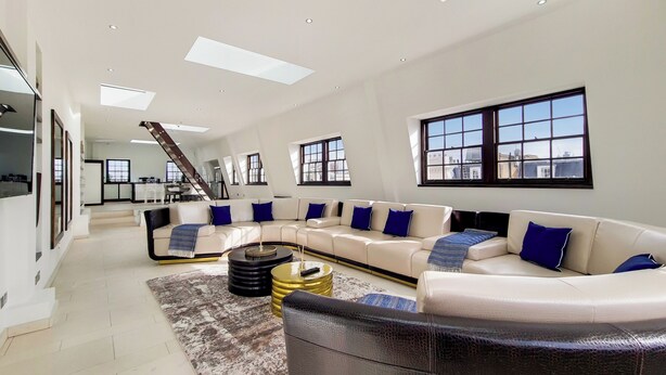 A spacious living room with a large sectional sofa, a coffee table, and a staircase leading to an upper level. - The Chesham Residences (London)