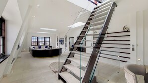 A modern interior with a glass staircase, a round seating area, and a high ceiling with skylights. - The Chesham Residences (London)