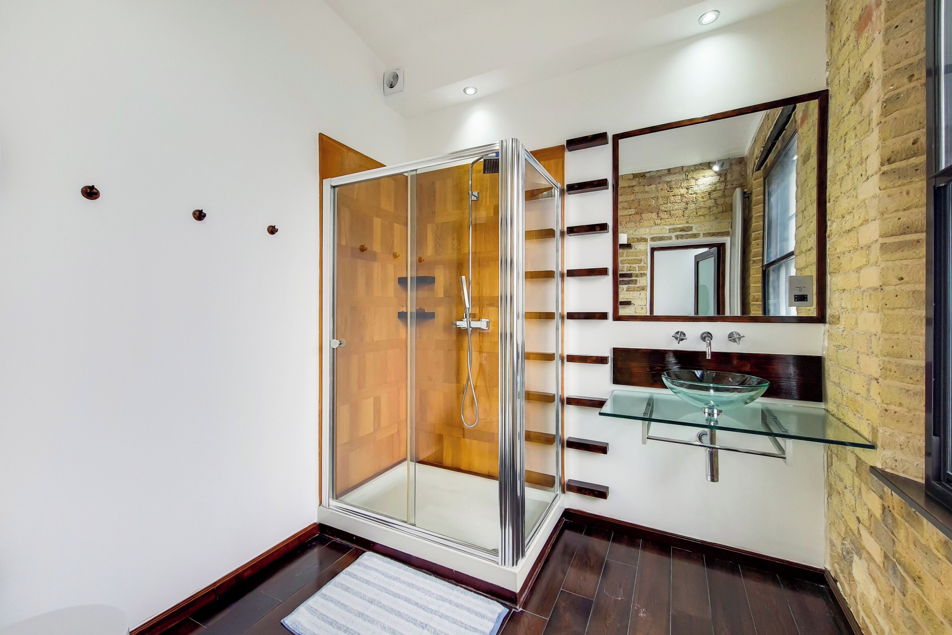 A modern bathroom with a glass-enclosed shower, a glass sink, and a mirror above it.