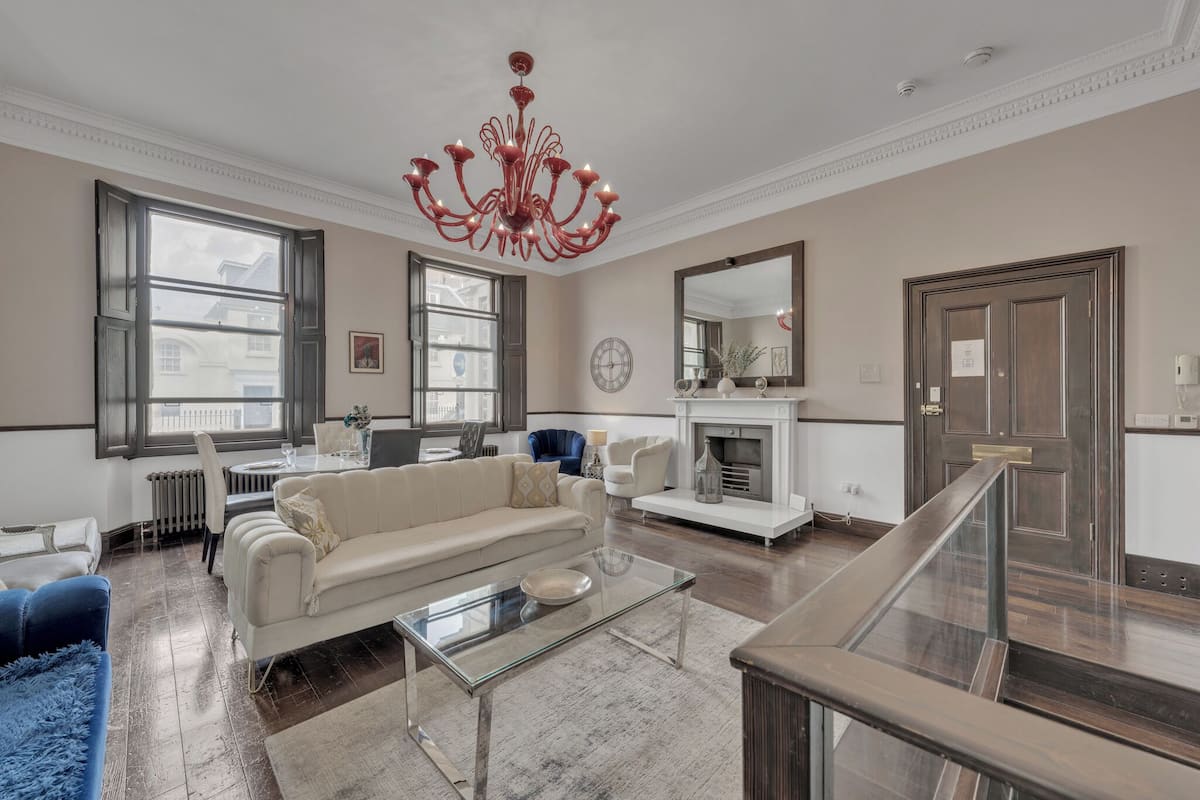 A spacious living room with a large chandelier, a fireplace, and a view of the city through large windows.