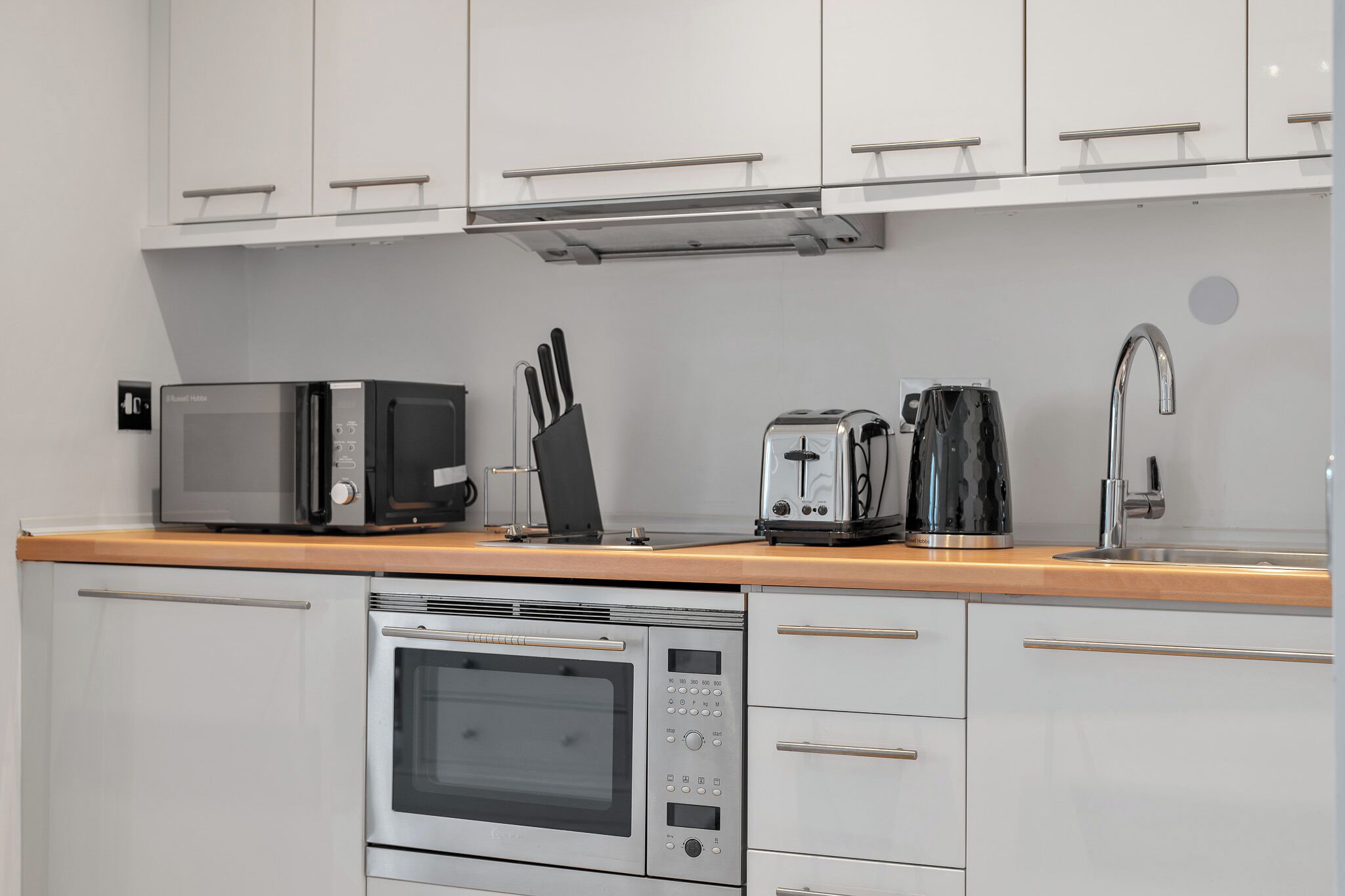 Cozinha moderna com armários brancos, eletrodomésticos de aço inoxidável, micro-ondas, torradeira, cafeteira e pia.