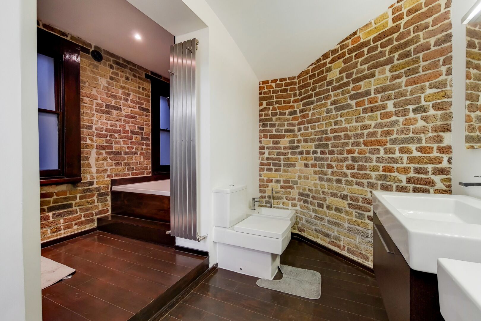Een badkamer met een bakstenen muur, een wit toilet en een witte wastafel.