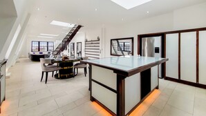 A spacious, modern kitchen with a central island, a dining area with a round table, and a staircase leading to an upper level. - The Chesham Residences (London)