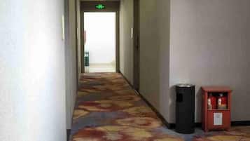 A hotel hallway with a carpeted floor, a trash bin, and a small cabinet with items on it.