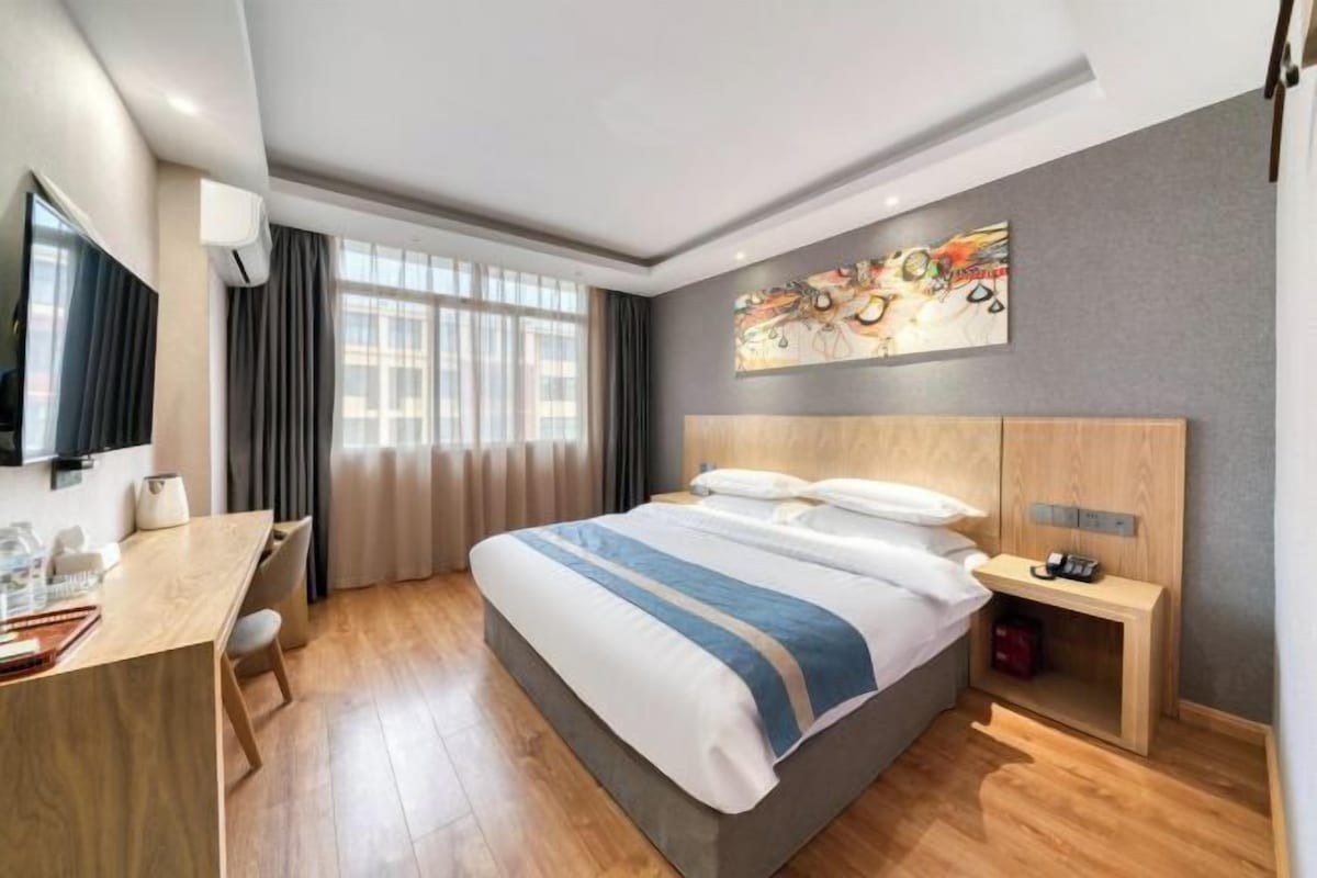 Une chambre d’hôtel avec un lit, un bureau, une chaise, une télévision, un tableau et une fenêtre.
