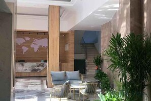 A lobby with a reception desk, seating area, staircase, and plants.