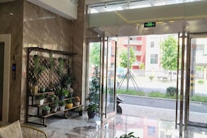 Un vestíbulo de hotel con suelo de mármol, un arreglo de plantas y puerta de entrada de vidrio.