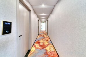 Un couloir d’hôtel avec un panneau numérique, une moquette à motifs floraux et une porte au bout.
